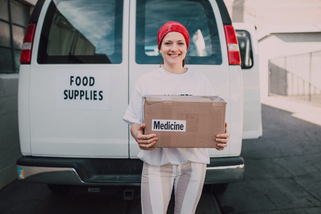 Woman Carrying a Medicine Labelled Cardboard Boxes Behind a White Van // Healthier Veterans Today