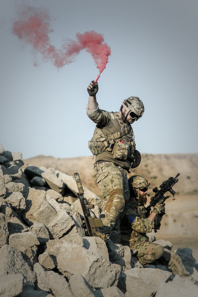 2 Soldier With Guns on Grey Pile of Rocks Holding Smoke Stick during Daytime // Healthier Veterans Today