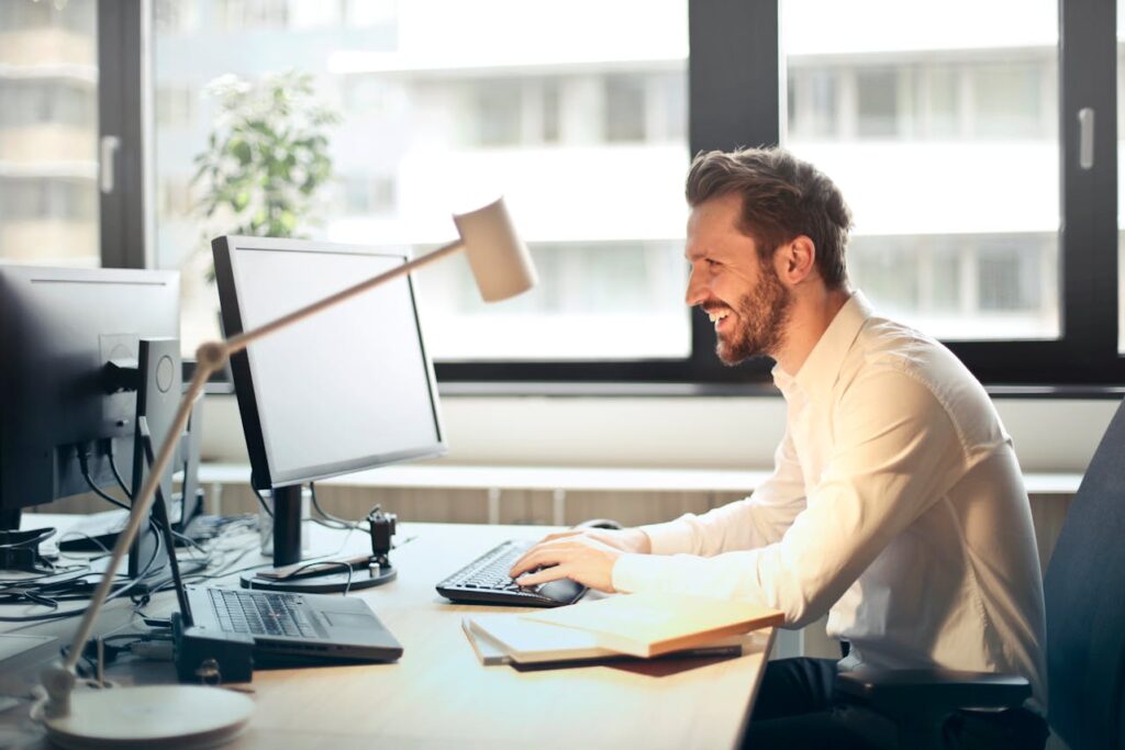 Man in White Dress Shirt Sitting on Black Rolling Chair While Facing Black Computer Set and Smiling // Healthier Veterans Today